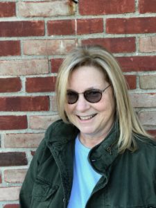 Woman in sunglasses smiling by brick wall.